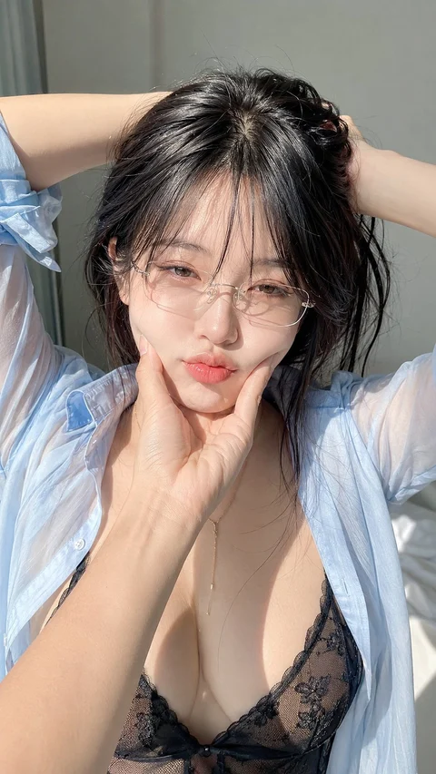 A woman with glasses poses with a finger on her cheek, wearing an open striped shirt over a dark top.